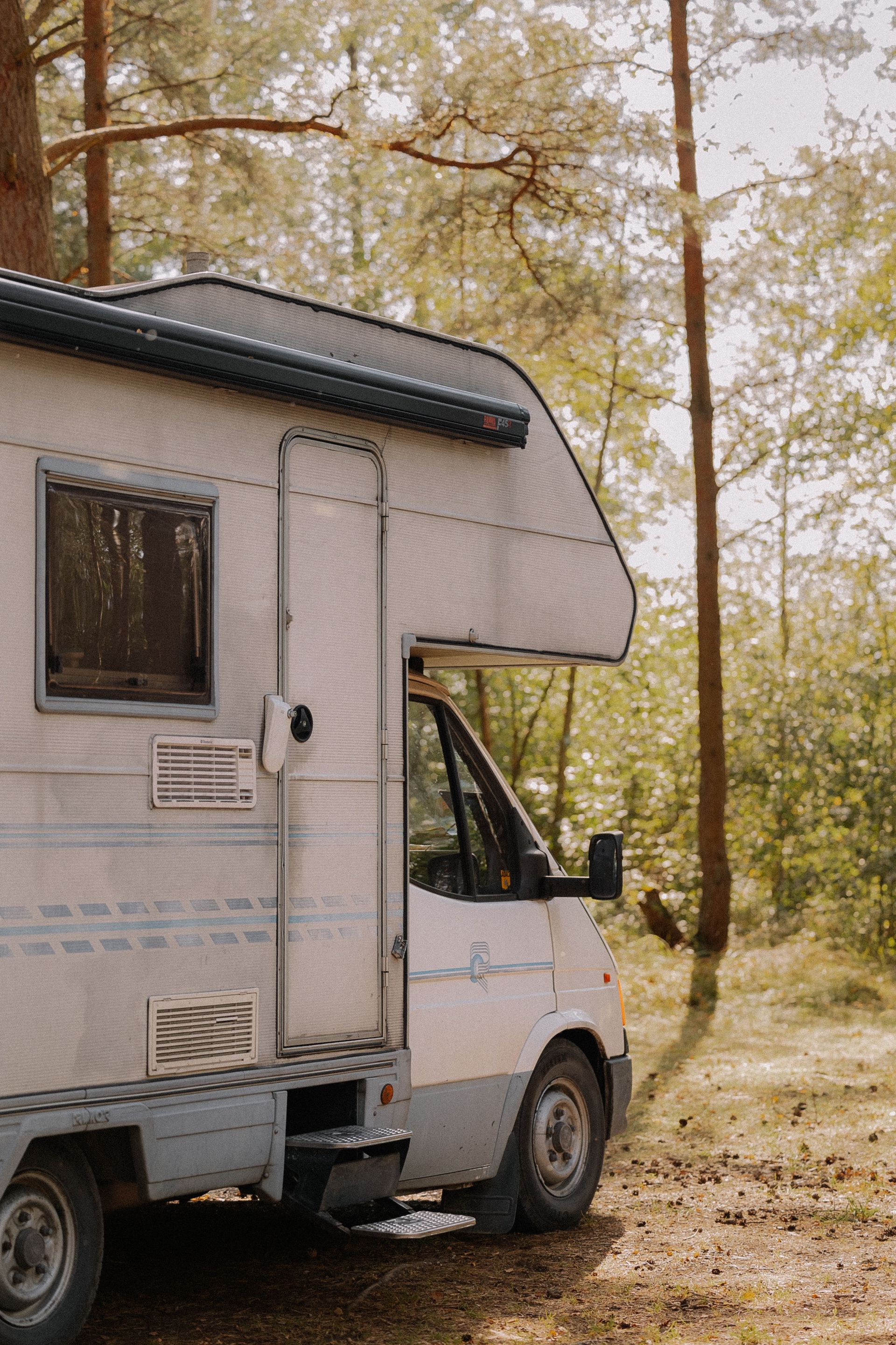 A serene image of a camper van parked in a sunlit forest, ideal for travel and adventure themes.